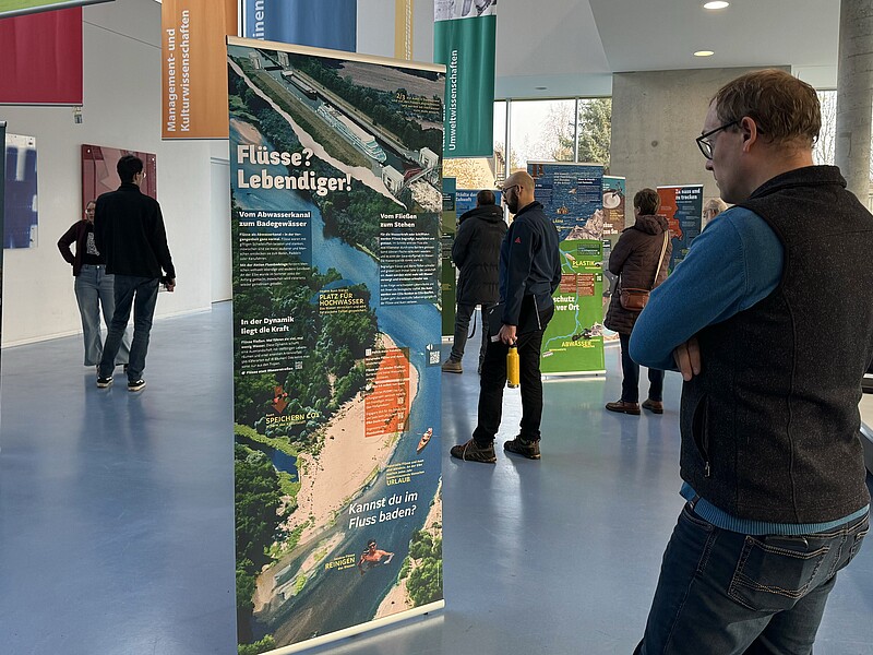 Ein Besucher steht vor einem Roll-up im Foyer von Haus Z Vier, umgeben von anderen Besuchenden der Ausstellung.