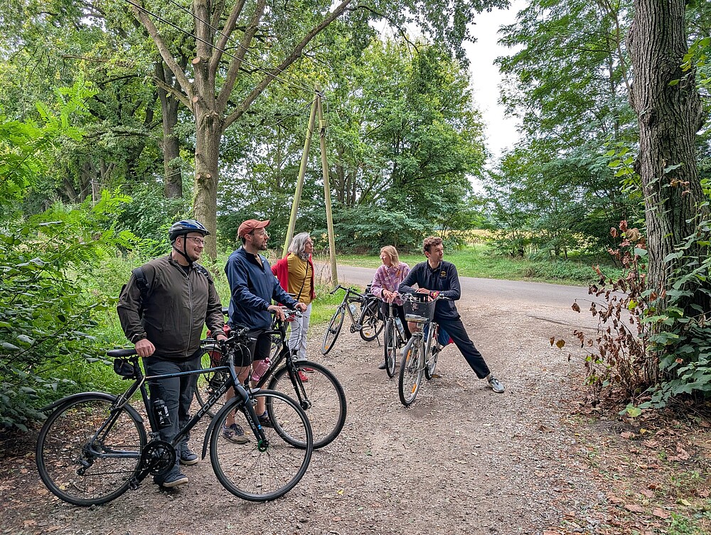 [Translate to Englisch:] 5 Menschen stehen mit ihren Fahrrädern zwischen Bäumen im Grünen