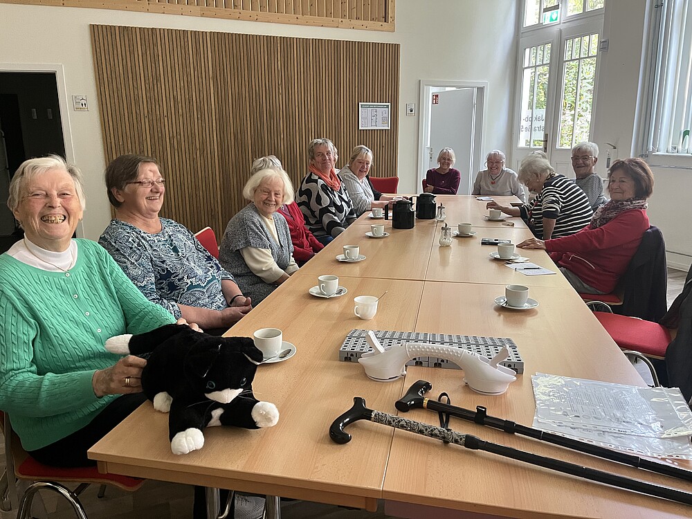 [Translate to Englisch:] Viele ältere Damen sitzen um einen großen Tisch mit verschiedenen technischen Hilfsmitteln