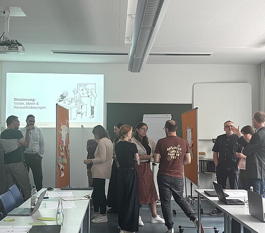 [Translate to Englisch:] Teilnehmer stehen um Pinnwände und tauschen sich aus