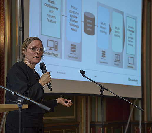 Eine Teilnehmerin steht vor einer digitalen Leinwand und richtet Worte an das Publikum.