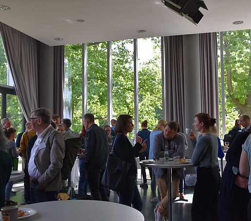 [Translate to Englisch:] Gruppe in der Aula mit Blick nach Draußen ins Grüne