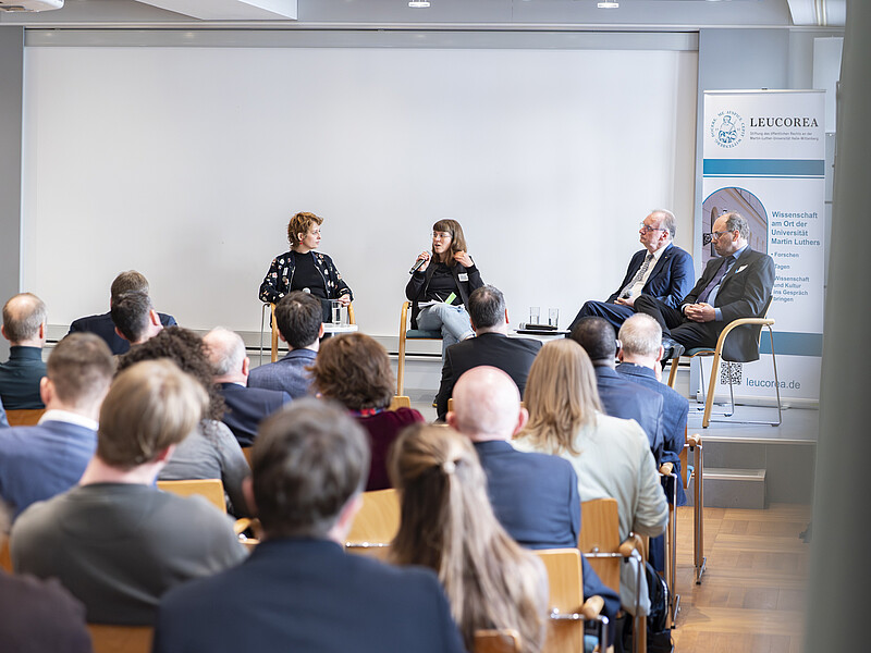 [Translate to Englisch:] Podium mit 4 Personen vor Zuschauern