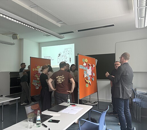 [Translate to Englisch:] Teilnehmer stehen um Pinnwände und tauschen sich aus