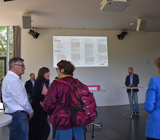 [Translate to Englisch:] Teilnehmer in der Aula schauen auf die Projektionswand und hören einem Redner zu