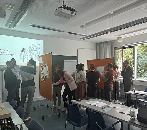 [Translate to Englisch:] Teilnehmer stehen um Pinnwände und tauschen sich aus