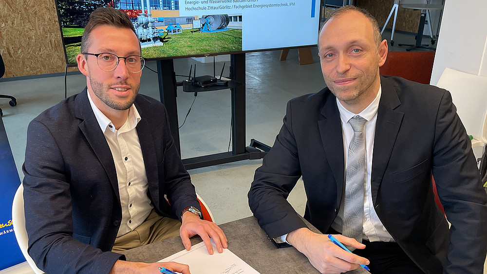 Der Bereichsleiter der EWB und Prof. Kunick von der HSZG unterzeichnen an einem Tisch die Kooperationsvereinbarung.