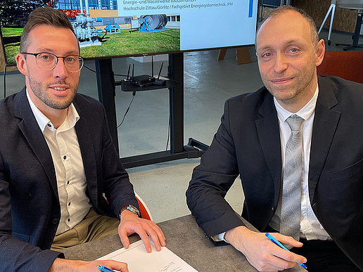Der Bereichsleiter der EWB und Prof. Kunick von der HSZG unterzeichnen an einem Tisch die Kooperationsvereinbarung.